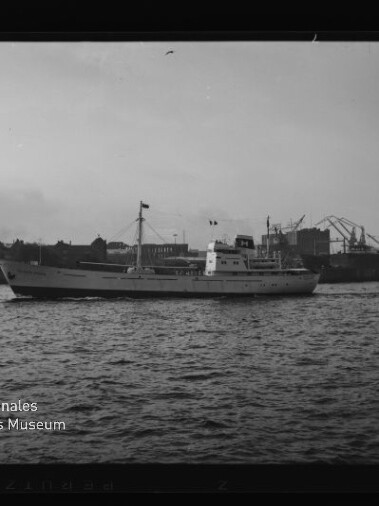 Weißes Frachtschiff auf ruhigem Wasser vor Hafen mit Kränen; schwarzweißes Foto mit Museumswasserzeichen.