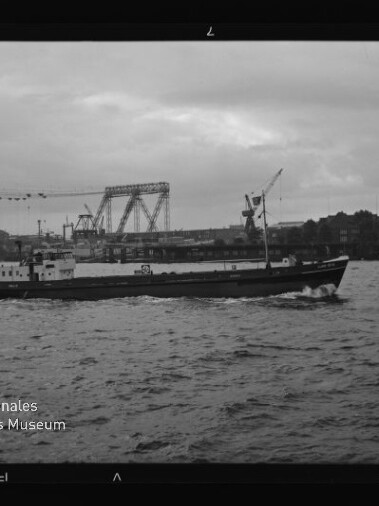 Frachtschiff auf bewegter See vor Industriehafen mit Kränen und Hubbrücke, Schriftzug 'Internationales Maritimes Museum Hamburg'.