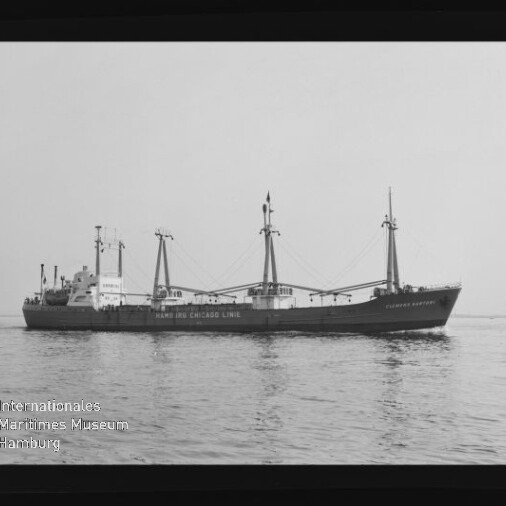 Frachtschiff mit drei Masten und Ladegeschirr auf ruhiger See; Wasserzeichen Internationales Maritimes Museum Hamburg unten