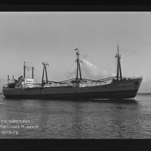 Schwarzweißaufnahme eines Frachtschiffs mit drei Ladebäumen auf ruhigem Meer; Wasserzeichen Internationales Maritimes Museum Hamburg
