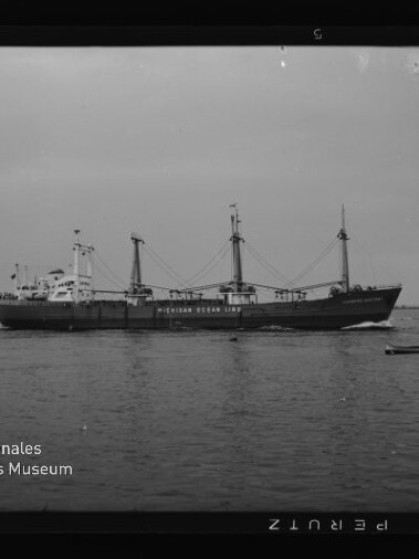Frachtschiff der Indian Ocean Line auf ruhigem Wasser, ein kleines Segelboot daneben und weitere Schiffe am Horizont.