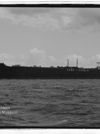 Schwarzweißfoto eines großen Tankers mit der Aufschrift VEBA‑CHEMIE auf dem Rumpf, auf offener See mit Museumslogo unten links.