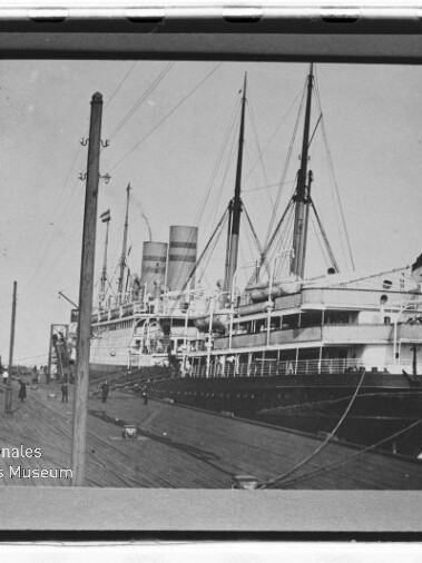 Großes Dampfschiff mit zwei Schornsteinen und Masten am Kai, Personen auf Pier; Wasserzeichen Int. Maritimes Museum Hamburg