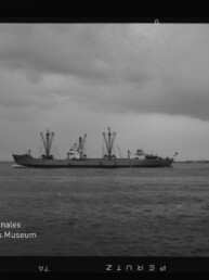 Frachtschiff mit Deckkränen fährt auf ruhigem Meer unter bewölktem Himmel; Museumslogo Internationales Maritimes Museum Hamburg unten links.