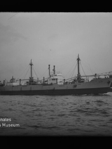 Schwarzweißfoto eines Frachtschiffs im Hafen mit Krananlage am rechten Bildrand und sichtbarem Museumslogo.