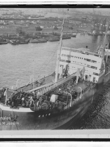 Großes Frachtschiff mit sichtbarem Namenszug 'Clio' fährt in einen Hafen mit Kränen; Museumswasserzeichen unten links.