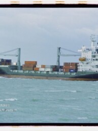 Frachtschiff mit Containern und zwei Ladekranen auf offener See; Wasserzeichen Internationales Maritimes Museum Hamburg.