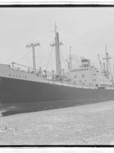 Frachtschiff CLIVIA mit mehreren Masten und Ladekränen liegt längsseits am Hafenquai.