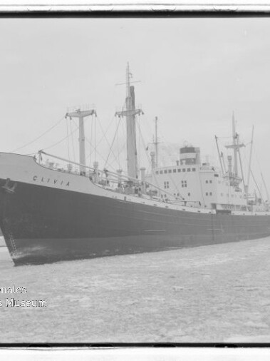 Großes Frachtschiff im Hafen mit sichtbarem Namen am Bug, Kaianlagen und Kräne im Hintergrund.