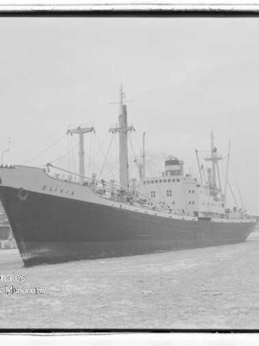 Frachtschiff Olivia längs Kai in einem Hafen, Kräne im Hintergrund und vereiste Wasseroberfläche.