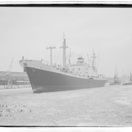 Großes Frachtschiff am Kai eines winterlichen Hafens mit Eis auf dem Wasser und Kränen im Hintergrund.