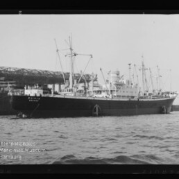 Frachtschiff Oliva am Kai vor einer Hafenanlage mit Kränen und Wasser im Vordergrund