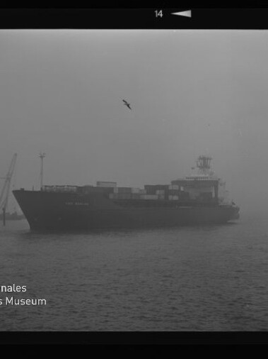 Containerschiff fährt durch dichten Nebel im Hafen, Container auf Deck, Möwen am Himmel und Museumslogo links unten