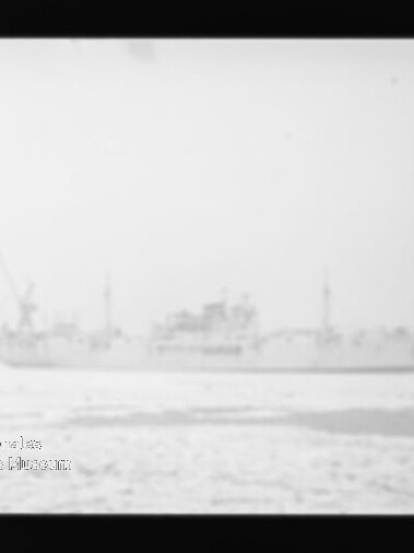 Verschwommenes Schwarzweißbild eines großen Schiffs im Hafen vor Kränen, mit Wasser im Vordergrund und Museumslogo links unten.