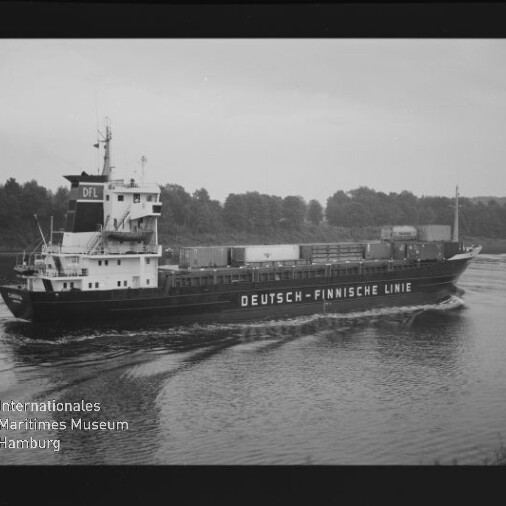 Frachtschiff mit Aufschrift DEUTSCH-FINNISCHE LINIE auf ruhigem Wasser vor einer Baumreihe; Schwarzweißaufnahme mit Museumslogo.