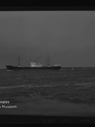 Frachtschiff mittig auf ruhiger See, kleines Segelboot rechts und Wasserzeichen Internationales Maritimes Museum links.