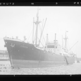 Frachtschiff COBURG am Kai, seitlich aufgenommen, mit Masten und Ladekränen, Schwarzweißfoto.