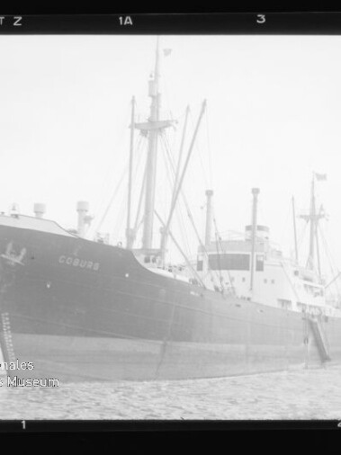 Frachtschiff COBURG am Kai, seitlich aufgenommen, mit Masten und Ladekränen, Schwarzweißfoto.