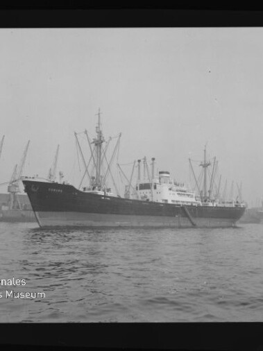 Frachtschiff mit Ladegeschirr auf dem Wasser vor Hafenkränen; Museumslogo und Schriftzug unten links.