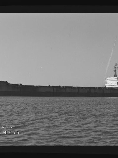 Großes Frachtschiff in Seitenansicht auf ruhiger See, schwarzweiß, mit Museumslogo unten links.