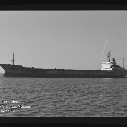Großes Frachtschiff in Seitenansicht auf ruhiger See, schwarzweiß, mit Museumslogo unten links.