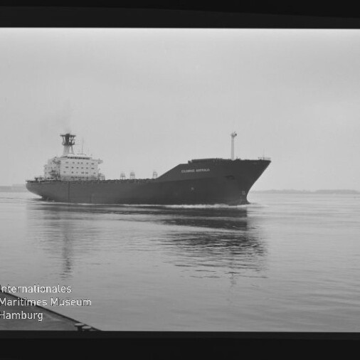 Schwarzweißaufnahme eines großen Frachtschiffs mit dem Namen „Columbus Australia“ auf ruhigem Wasser, leichte Spiegelung im Vordergrund, weiter flacher Horizont und Museumswasserzeichen unten links.
