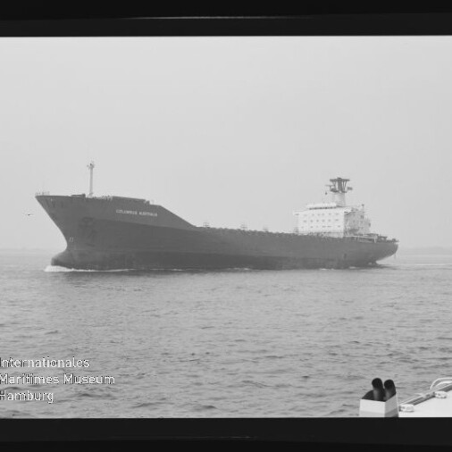 Schwarzweißaufnahme eines großen Tankschiffs mit Aufbauten achtern, das auf ruhiger See fährt; rechts im Vordergrund ein Schiffsdeck mit Poller und links unten ein Wasserzeichen des Internationalen Maritimen Museums Hamburg.