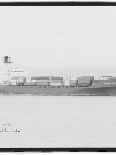 Seitenansicht eines beladenen Containerschiffs, das ruhig auf dem Meer fährt, mit übereinander gestapelten Containern und einem Museumsstempel unten links (Internationales Maritimes Museum Hamburg).