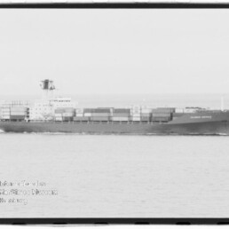 Schwarzweiß-Aufnahme eines langen Containerschiffs in Seitenansicht auf ruhiger See mit gestapelten Containern und Aufbauten mittschiffs; Museumslogo des Internationalen Maritimen Museums Hamburg unten links.