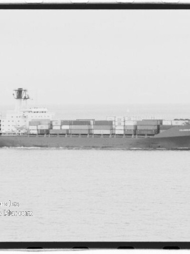 Schwarzweiß-Aufnahme eines langen Containerschiffs in Seitenansicht auf ruhiger See mit gestapelten Containern und Aufbauten mittschiffs; Museumslogo des Internationalen Maritimen Museums Hamburg unten links.