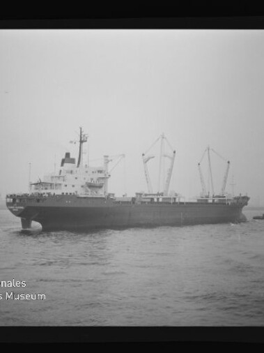 Schwarzweiß-Foto eines Frachtschiffs auf See mit drei sichtbaren Ladekränen und einem kleinen Begleitboot rechts, gerahmt als Filmnegativ mit Logo des Internationalen Maritimen Museums Hamburg.