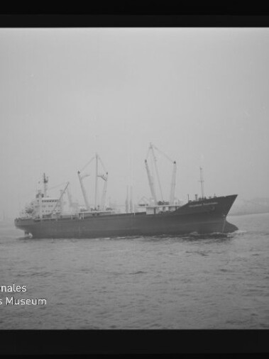 Schwarzweiß-Foto eines Frachtschiffs im Halbprofil mit mehreren Ladekränen auf ruhigem Wasser vor trübem Himmel; das Bild zeigt den Filmnegativ-Rahmen und unten links das Logo ‚Internationales Maritimes Museum Hamburg‘.