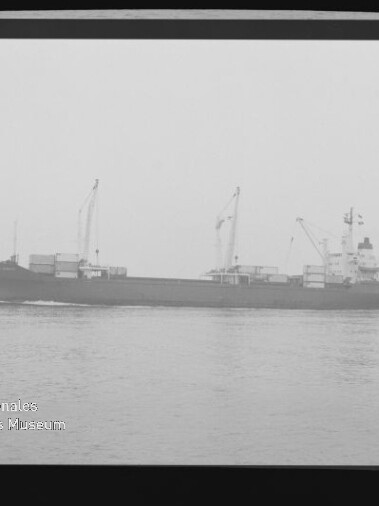 Schwarz-weiß-Fotografie eines Frachtschiffs in Seitenansicht auf ruhiger See mit mehreren Ladekränen an Bord; Filmrand mit 'KODAK'-Schriftzug und Wasserzeichen des Internationalen Maritimen Museums Hamburg.