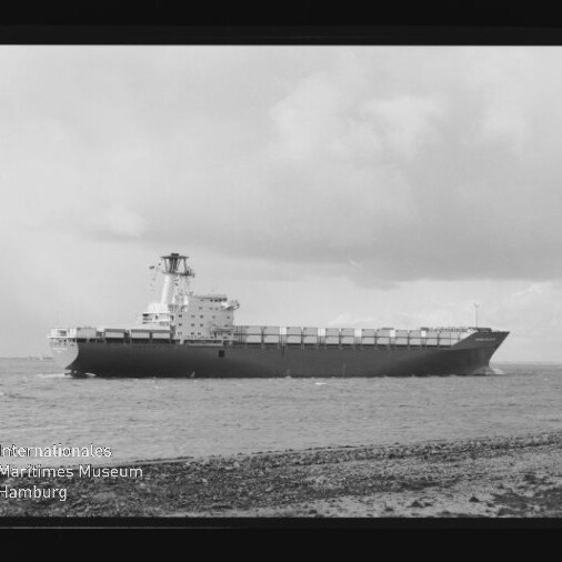 Schwarzweißaufnahme eines großen Containerschiffs in Seitenansicht auf ruhiger See, im Vordergrund ein Kiesstrand mit zwei kleinen Personen rechts, wolkiger Himmel und links unten das Signet Internationales Maritimes Museum Hamburg.