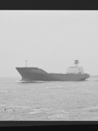 Schwarzweißaufnahme eines großen Frachtschiffs, das auf ruhiger See nahe dem Horizont fährt, mit sichtbarem Filmrand (AGFA PAN 400) und Museumswasserzeichen unten links.