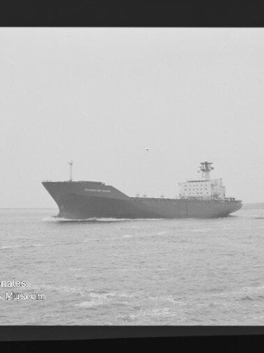 Schwarzweißaufnahme eines großen Frachtschiffs, das auf ruhiger See nahe dem Horizont fährt, mit sichtbarem Filmrand (AGFA PAN 400) und Museumswasserzeichen unten links.