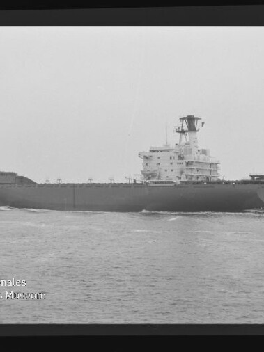 Schwarz‑weiß-Foto eines großen Frachtschiffs auf ruhiger See, seitliche Aufnahme mit hohem Brückenaufbau und Mast; Filmrand und Wasserzeichen des Internationalen Maritimen Museums Hamburg links unten sichtbar.
