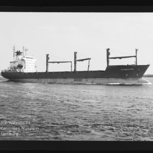 Schwarzweiß-Foto eines großen Frachtschiffs mit drei Ladekranen, das bei ruhiger See parallel zum Bildrand fährt; unten links ein Wasserzeichen des Internationalen Maritimen Museums Hamburg.