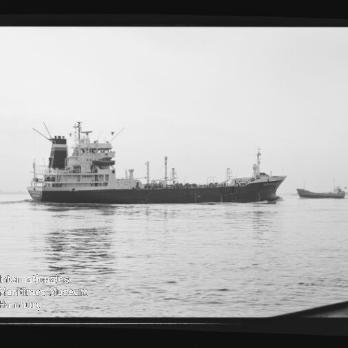 Schwarzweißaufnahme eines großen Tankers auf ruhiger See mit einer kleinen Begleitbarkasse rechts, gezeigt innerhalb eines Negativrahmens mit Filmkennzeichnung ‚AGFAPAN 100‘ und sichtbarem Museumswasserzeichen unten links.