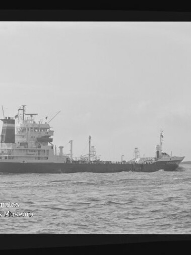 Schwarz-weiß-Foto eines Frachtschiffes/Tankers in Seitenansicht auf ruhiger See mit sichtbaren Aufbauten und Ladeeinrichtungen, Wellen im Vordergrund und dem Wasserzeichen des Internationalen Maritimen Museums Hamburg unten links.