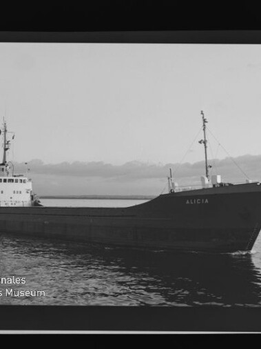 Schwarzweißbild eines Frachtschiffs mit dem Namen ALICIA, seitlich auf ruhiger See vor flachem, leicht bewölktem Horizont, fotografisch gerahmt mit Museumswasserzeichen.