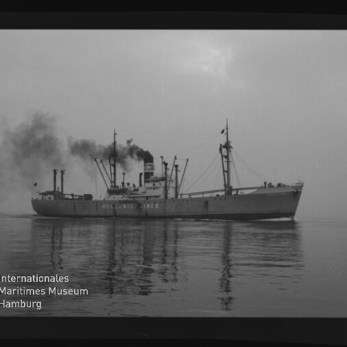 Schwarzweiß-Foto eines Frachtschiffs mit rauchendem Schornstein, Ladekränen und Spiegelung auf ruhiger See; unten links das Siegel des Internationalen Maritimen Museums Hamburg.