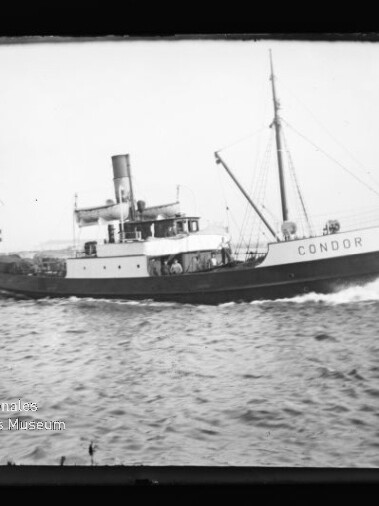 Schwarzweiß-Foto eines kleinen Dampfschiffs mit Schornstein, Mast und dem Namen „CONDOR“ am Vorschiff, das mit sichtbarer Bugwelle über das Meer fährt.
