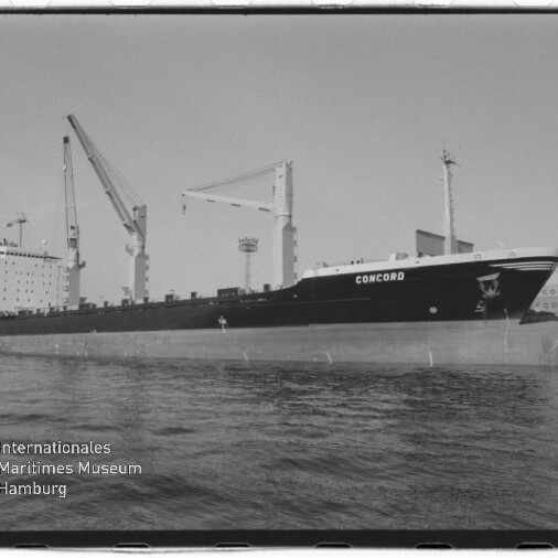 Schwarzweiß-Foto eines Frachtschiffs mit dem Namen CONCORD, längsseits im Hafen liegend mit mehreren Ladekränen an Deck, Hafenanlagen im Hintergrund und Wasser im Vordergrund, im unteren linken Eck das Logo des Internationalen Maritimen Museums Hamburg.