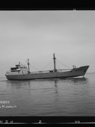 Schwarzweißfoto eines Frachtschiffs (Seitenansicht, Name „CONCORDIA“ am Bug) auf ruhiger See mit sichtbaren Masten, Ladegeschirr und leichtem Spiegelbild im Wasser; Filmrand und Museumswasserzeichen unten links erkennbar.