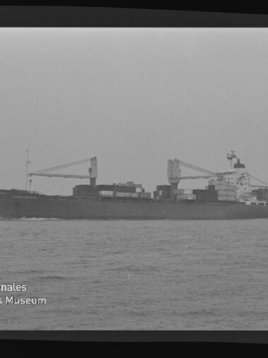 Seitliche Schwarzweißaufnahme eines Containerschiffs mit Ladekränen und gestapelten Containern auf ruhiger See unter grauem Himmel, mit Wasserzeichen Internationales Maritimes Museum Hamburg unten links.
