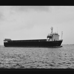 Schwarzweiß-Seitenaufnahme eines Frachtschiffs, das auf ruhiger See fährt, mit sichtbarer Brücke und Aufbauten sowie Filmrandmarkierungen und Wasserzeichen des Internationalen Maritimen Museums Hamburg.