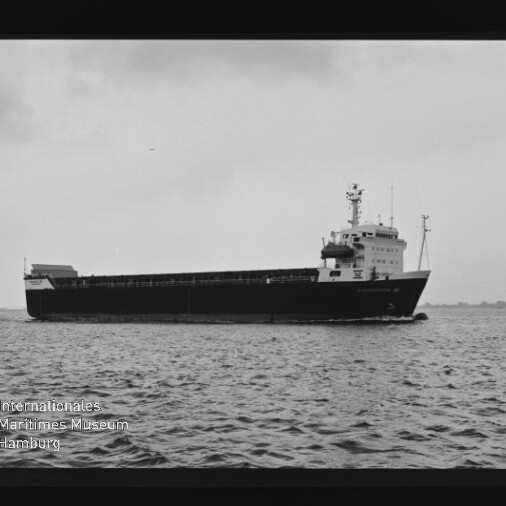 Schwarzweiß-Seitenaufnahme eines Frachtschiffs, das auf ruhiger See fährt, mit sichtbarer Brücke und Aufbauten sowie Filmrandmarkierungen und Wasserzeichen des Internationalen Maritimen Museums Hamburg.