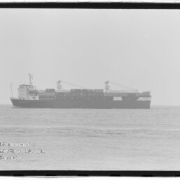 Schwarzweißaufnahme eines Containerschiffs mit zwei Deckskränen, seitlich auf ruhiger See fotografiert, mit Wasserzeichen des Internationalen Maritimen Museums Hamburg in der linken unteren Ecke.