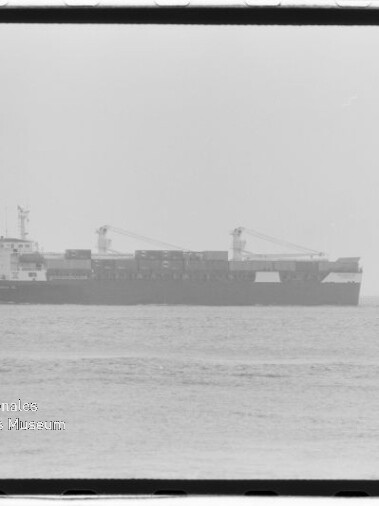 Schwarzweißaufnahme eines Containerschiffs mit zwei Deckskränen, seitlich auf ruhiger See fotografiert, mit Wasserzeichen des Internationalen Maritimen Museums Hamburg in der linken unteren Ecke.